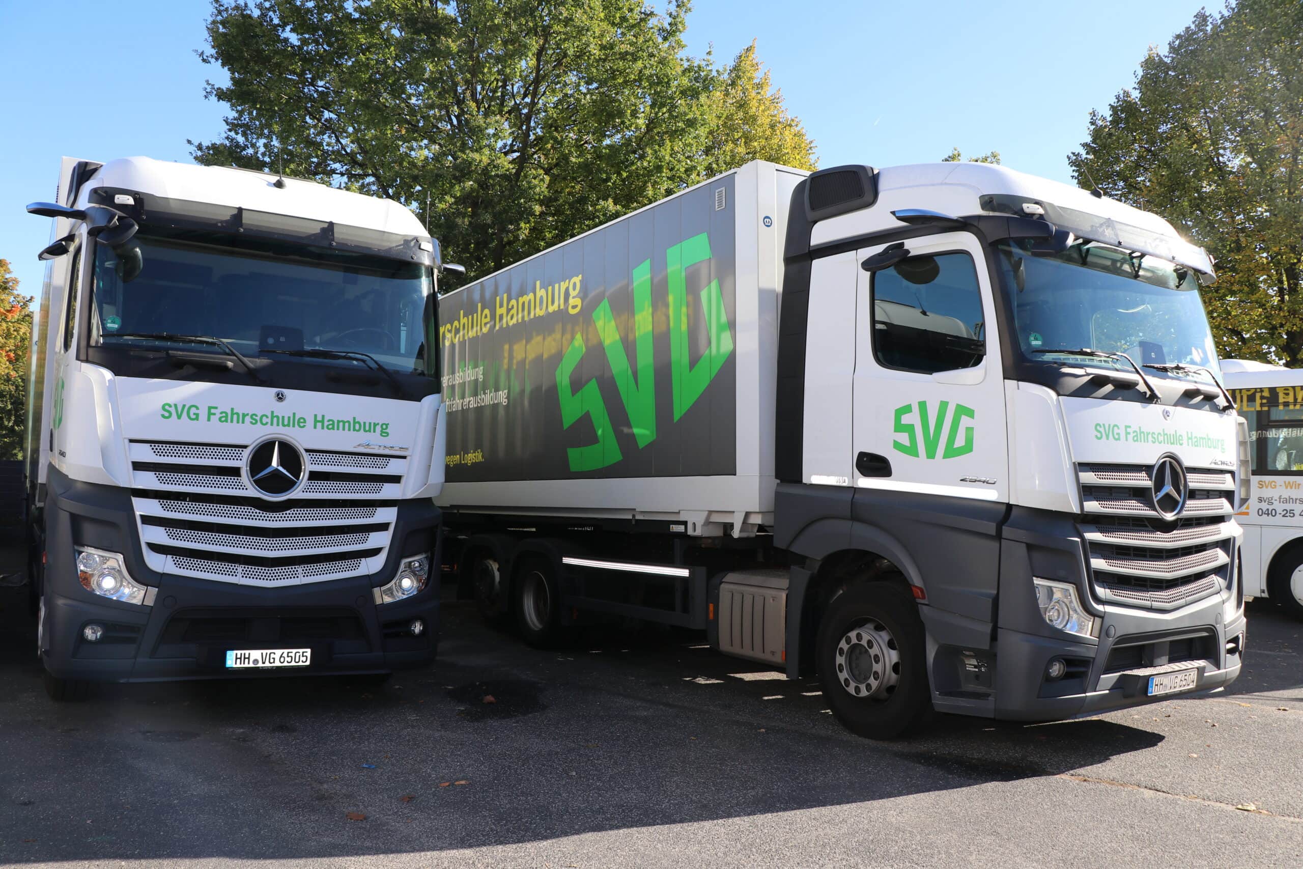 Zwei Lkw der "SVG Fahrschule Hamburg" in einem Parkplatz mit weißer und grüner Beschriftung.