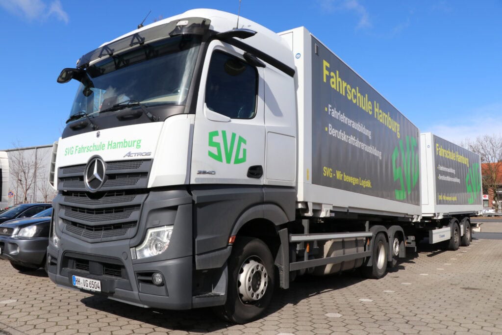 Lkw mit "Fahrschule Hamburg" Schriftzug, silber-grau, blauem Himmel, Seite zeigt grüne SVG-Logos.